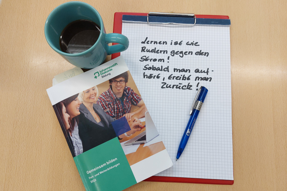 Teamomat: Kaffeetasse, Programmheft und Kladde mit beschriebenem Karopapier