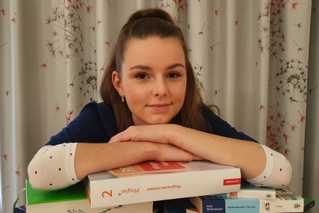 Teamomat: Junge Frau verschränkt Arme über einem Stapel Bücher